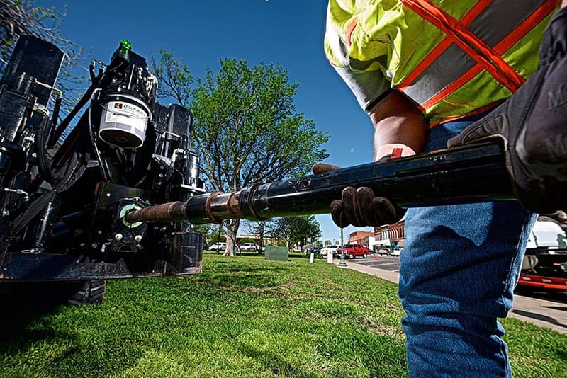Operator loading drill pipe into a horizontal directional drill beside a roadway